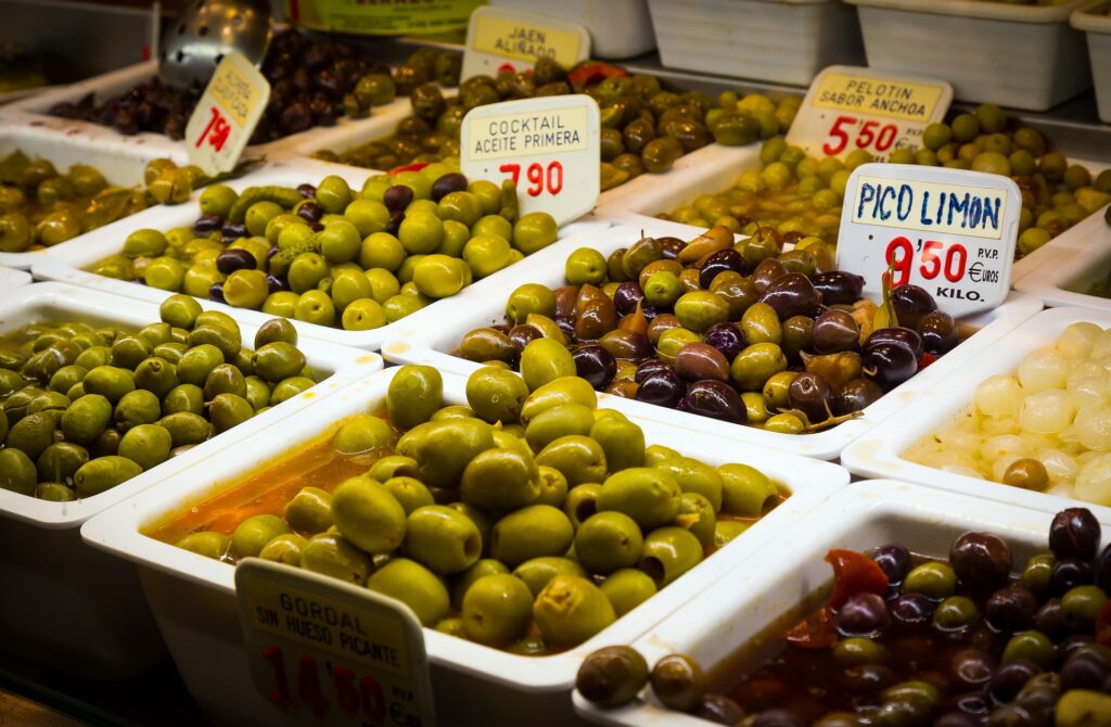 A vibrant stall at La Boqueria Market overflowing with dozens of olive varieties, from green to black, stuffed with peppers, garlic, and herbs.