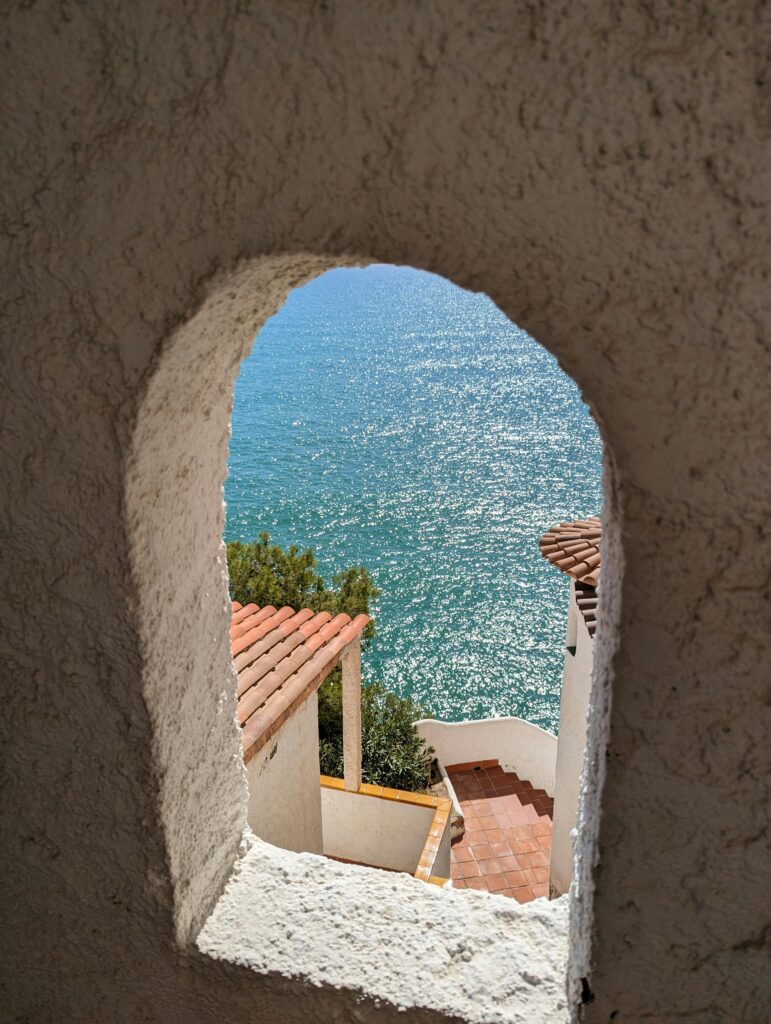 A glimpse of the shimmering sea through an architectural frame, revealing the timeless beauty of Sitges' shoreline