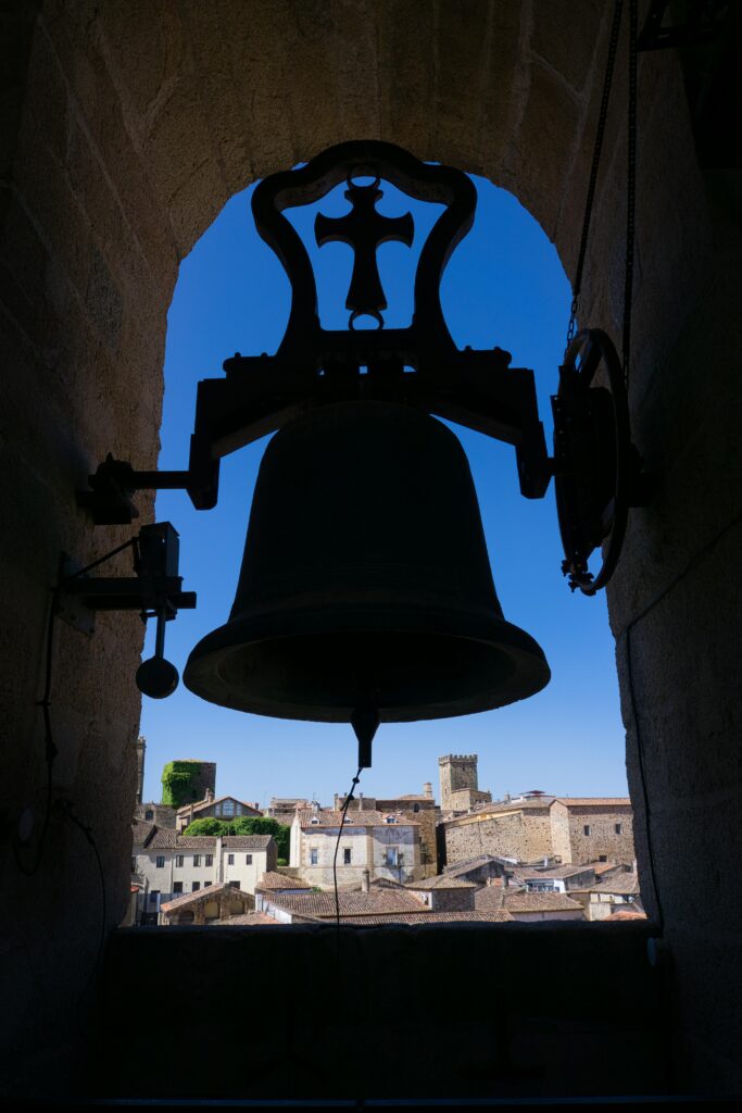 A church bell in a rustic bell tower, overlooking the rooftops of a peaceful village in Spain