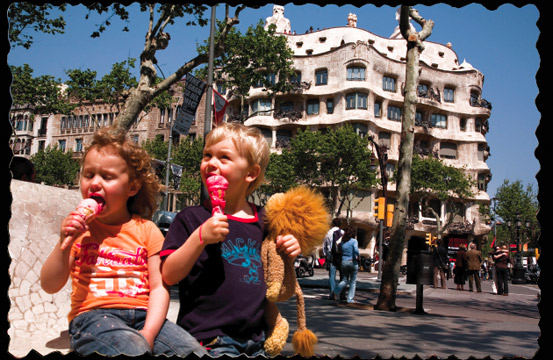 Two children happily eating ice cream on a sunny street near Barcelona's iconic La Pedrera building, enjoying a typical, cheerful city atmosphere.